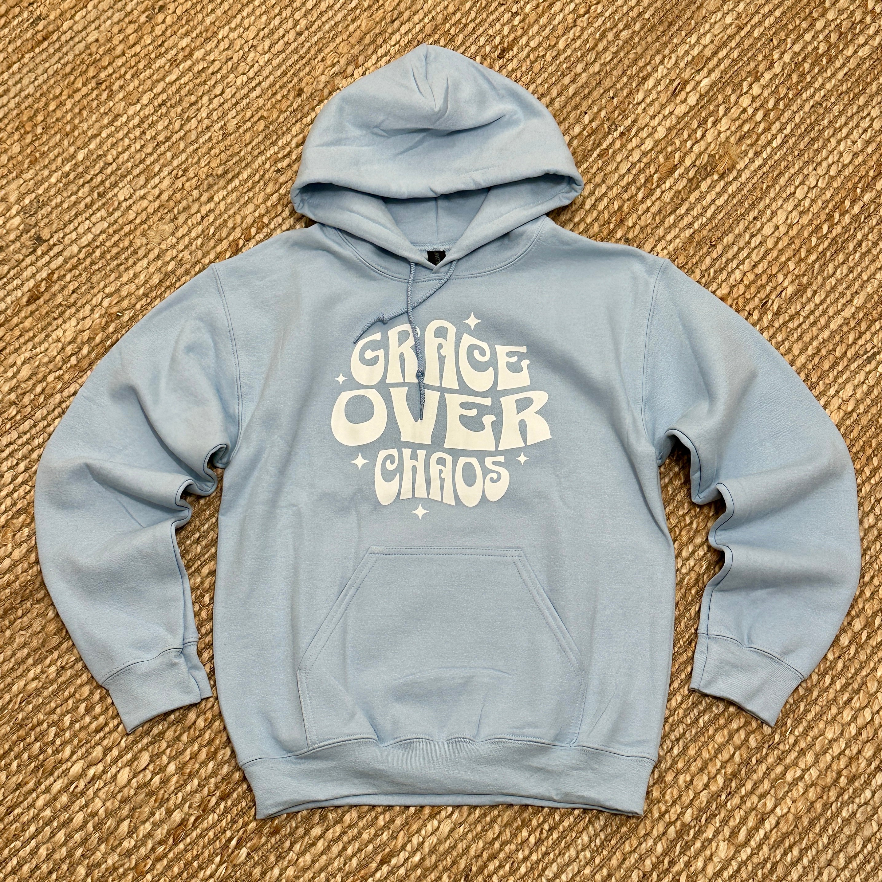 Light blue hoodie with 'Grace Over Chaos' text on a textured brown surface